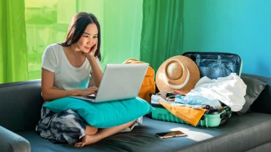 A woman on a laptop next to an unpacked suitcase