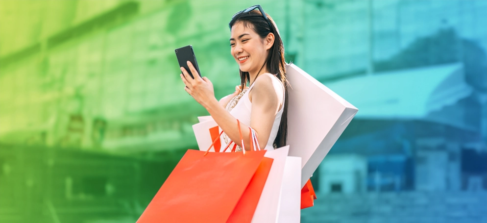 A woman checking her phone whilst carrying luxury shopping bags