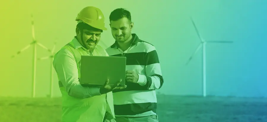 two men looking at laptop with wind turbines