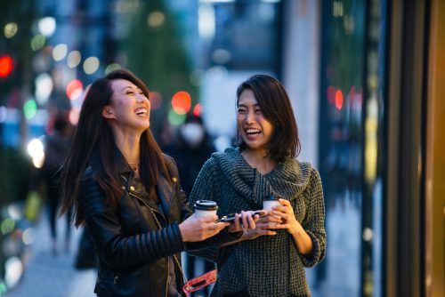 Two women laughing together holding coffee cups